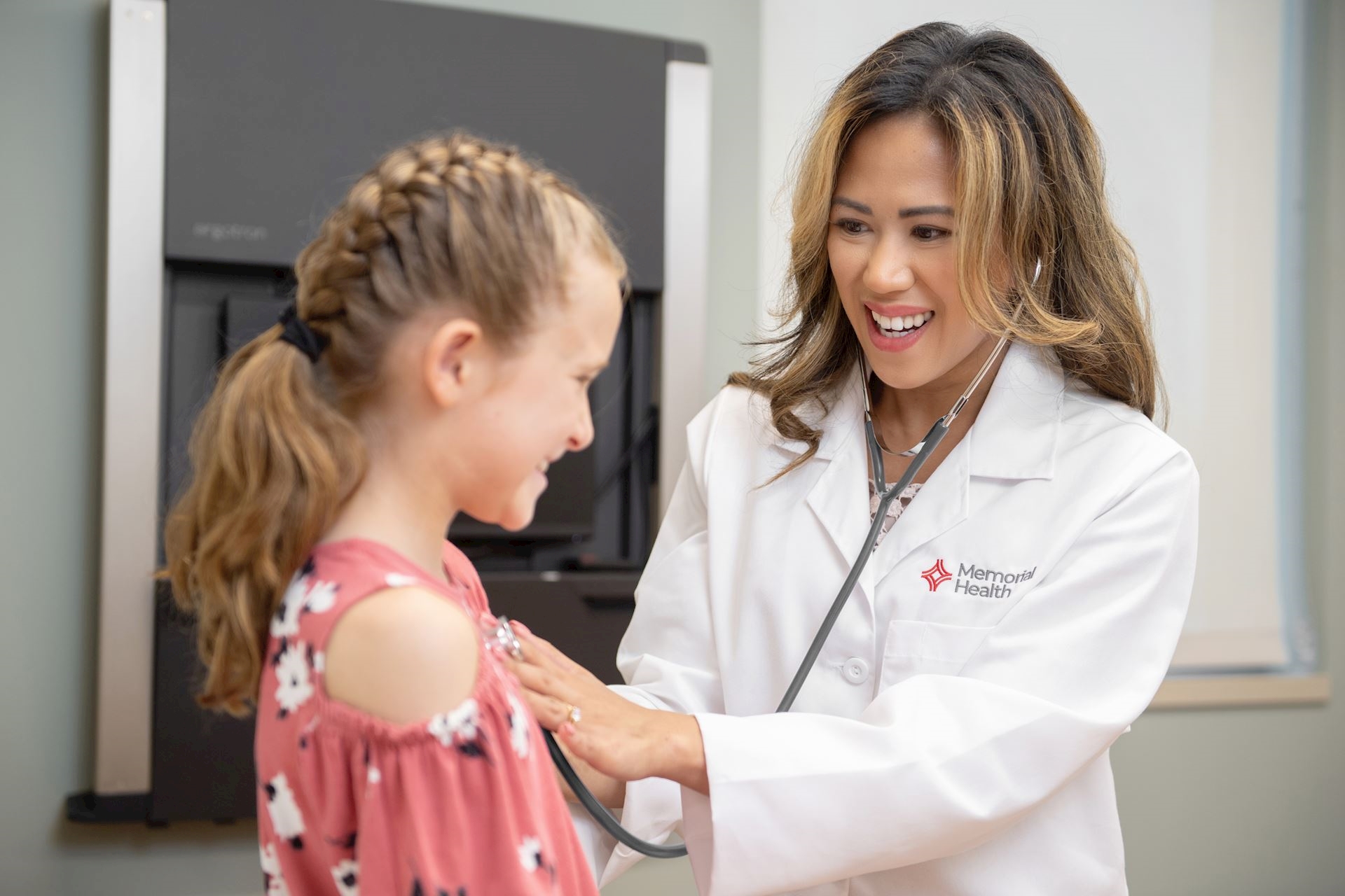 Dr. Bautista in a white coat listening to a child's heartbeat